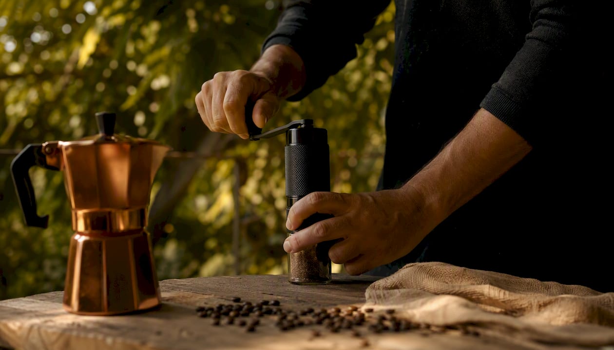 Hands grinding coffee next to moka pot